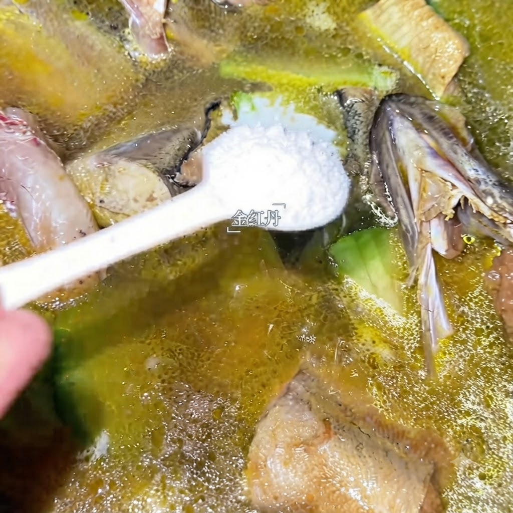 A spoonful of white seasoning being added into the simmering pot of pollack soup.