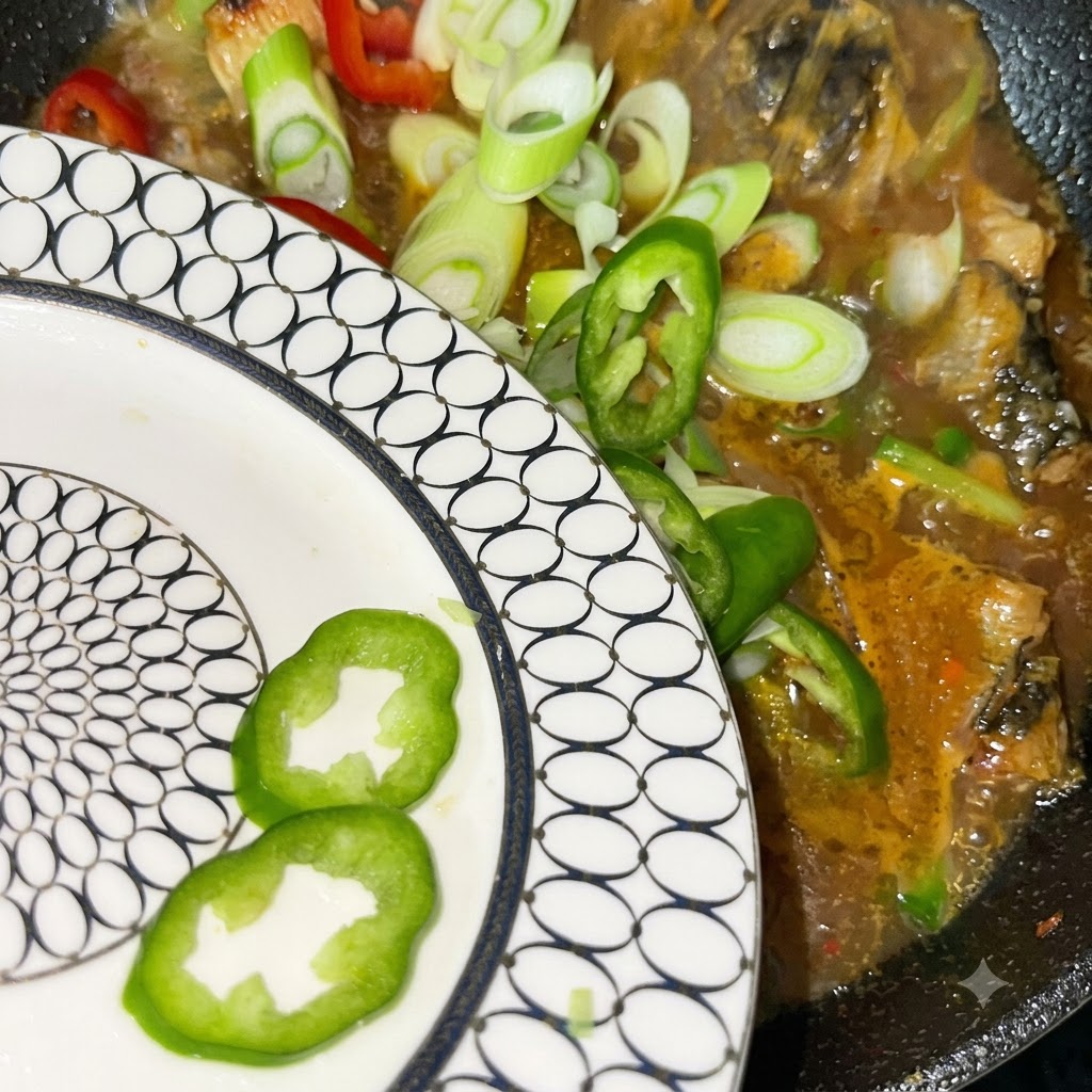 Freshly sliced green onions and red and green chili peppers being poured from a white patterned plate into the simmering pot.