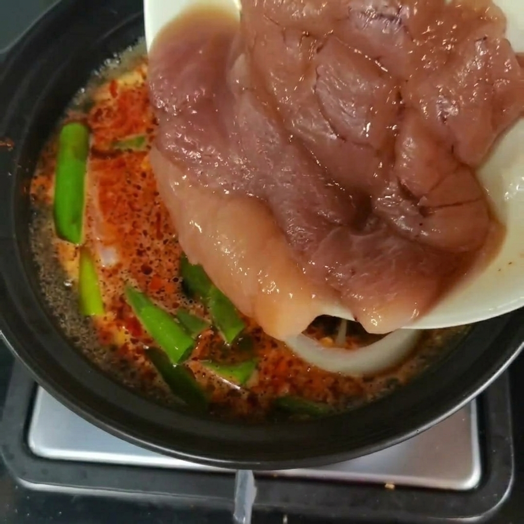 Fresh pieces of pollock roe being transferred from a plate into a pot of simmering soup with green vegetables.