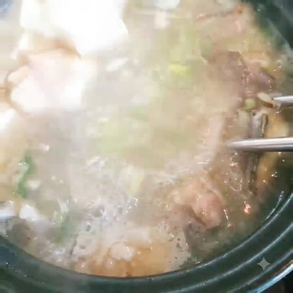 Tofu cubes being added to a pot of bubbling fish soup with green onions.