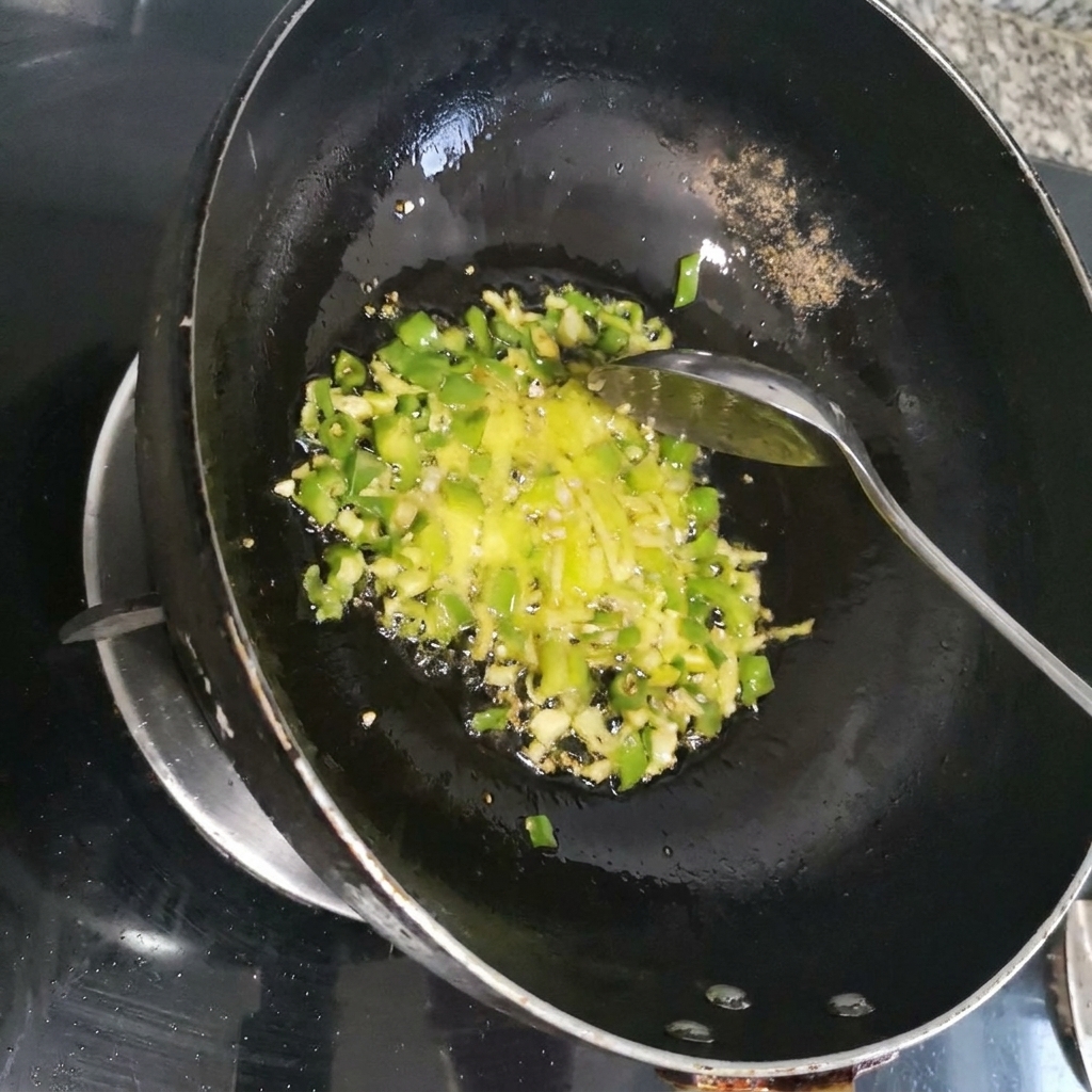 Shredded red chili being stir-fried with green aromatics inside a dark wok.