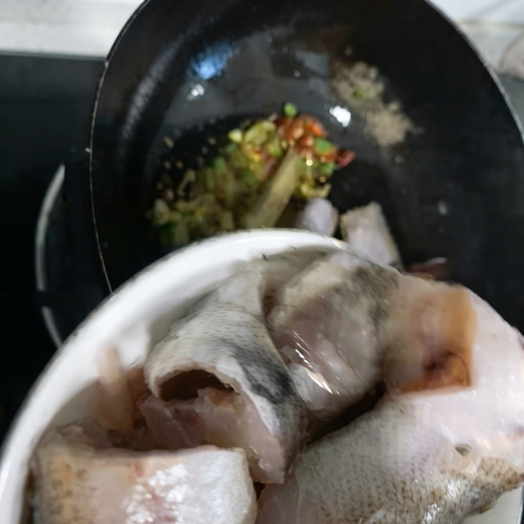 Pollock fish pieces being transferred from a bowl into the wok.