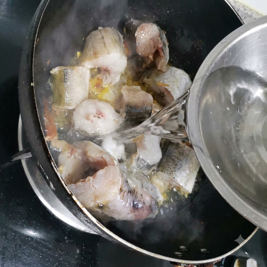 Water being poured from a metal bowl into the pan with the pollock pieces.