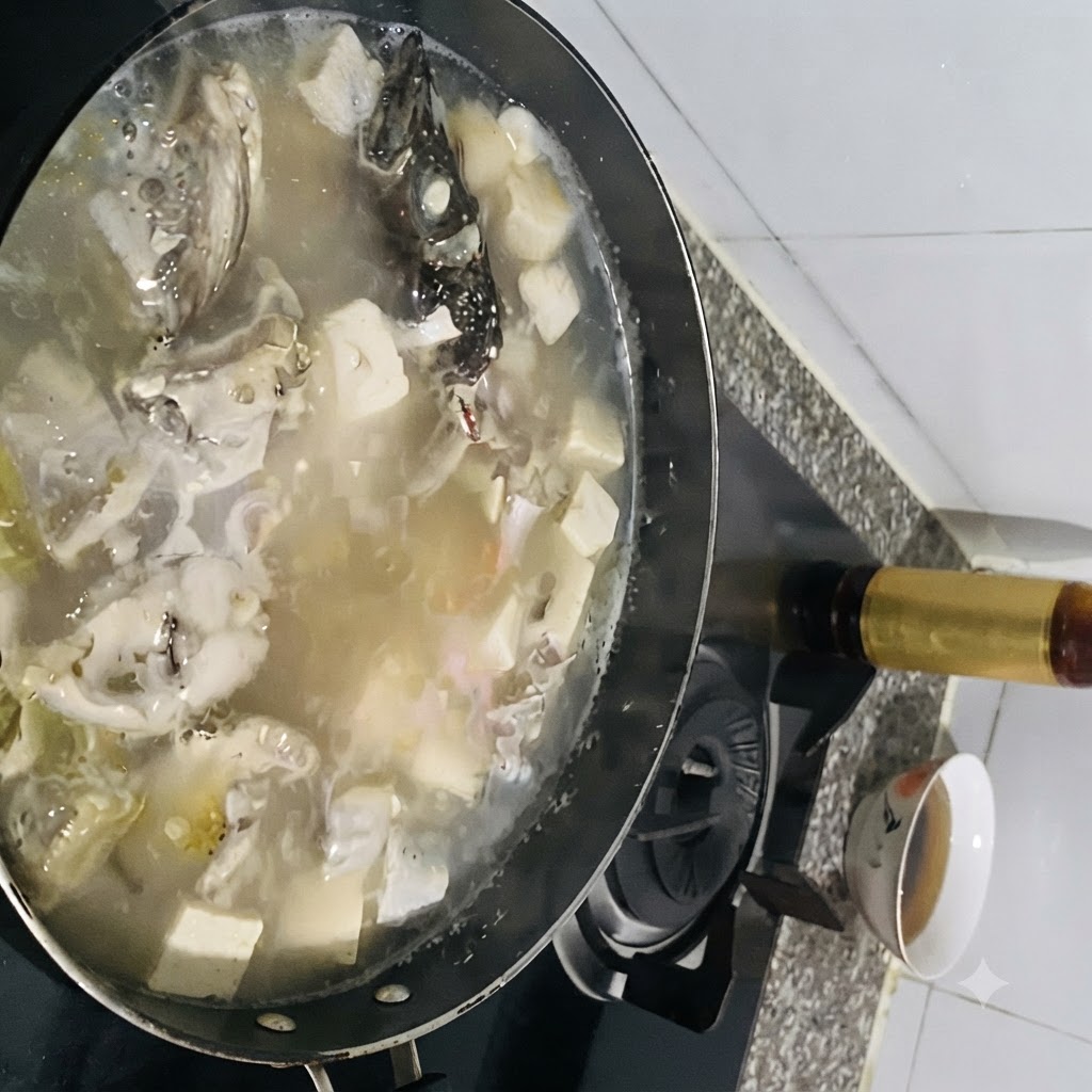 Seasonings being added to a bubbling pot of fish soup with tofu.