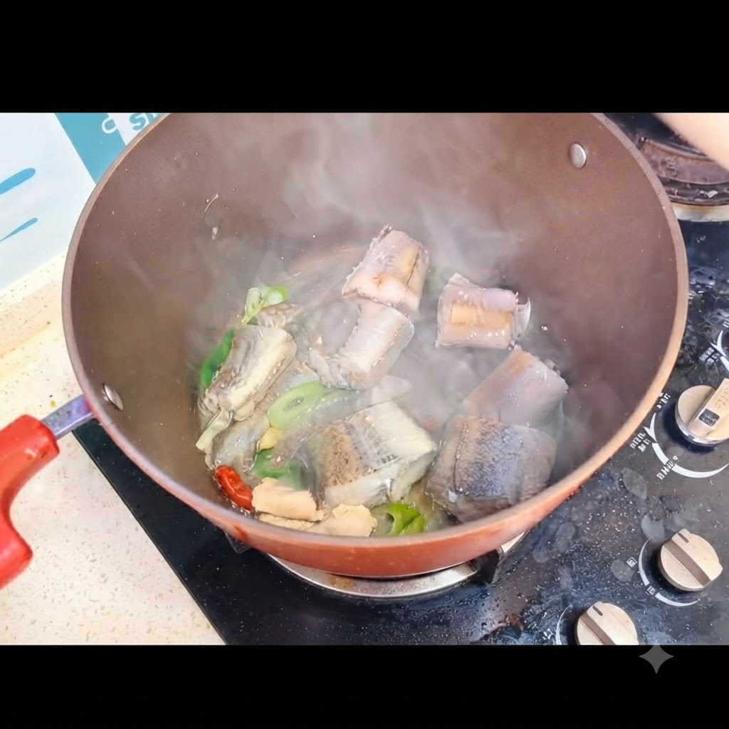 Boiling water being poured over fish pieces inside a cooking pot on a stove.
