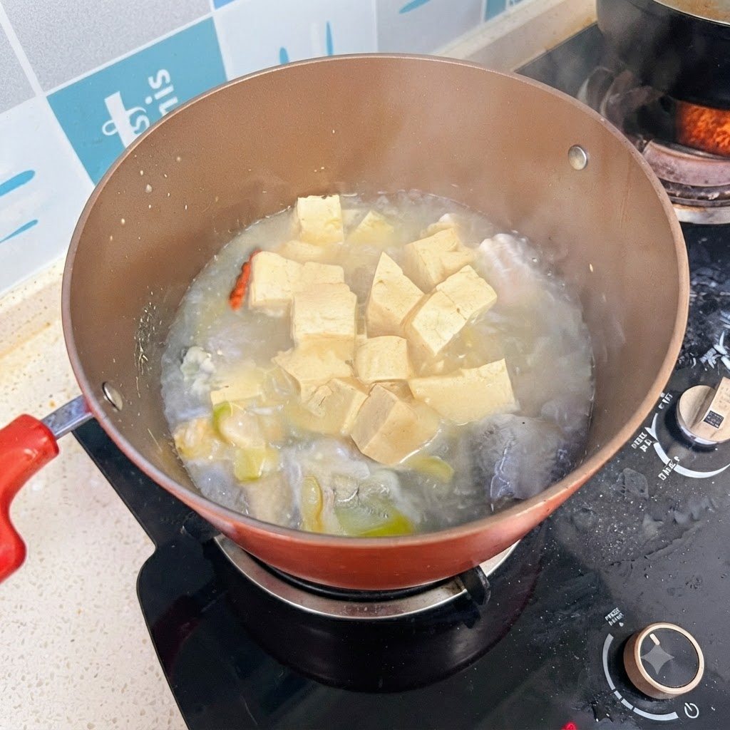 A pot of fish and tofu soup simmering on the stove with a milky white broth.