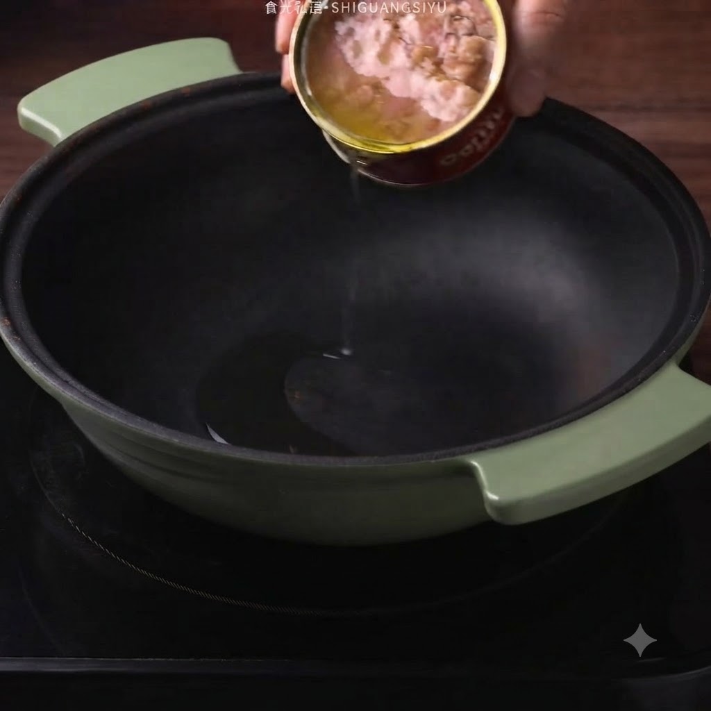 Canned tuna oil being poured from a can into a dark green pot.