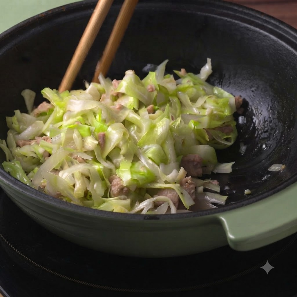 Wooden chopsticks mixing the cooked cabbage and tuna ingredients inside the pot.
