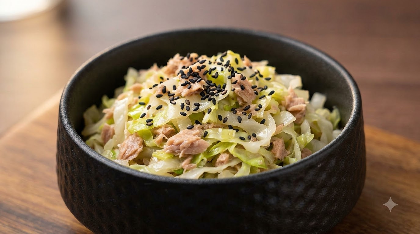 A small black bowl of savory braised cabbage and flaked tuna garnished with black sesame seeds
