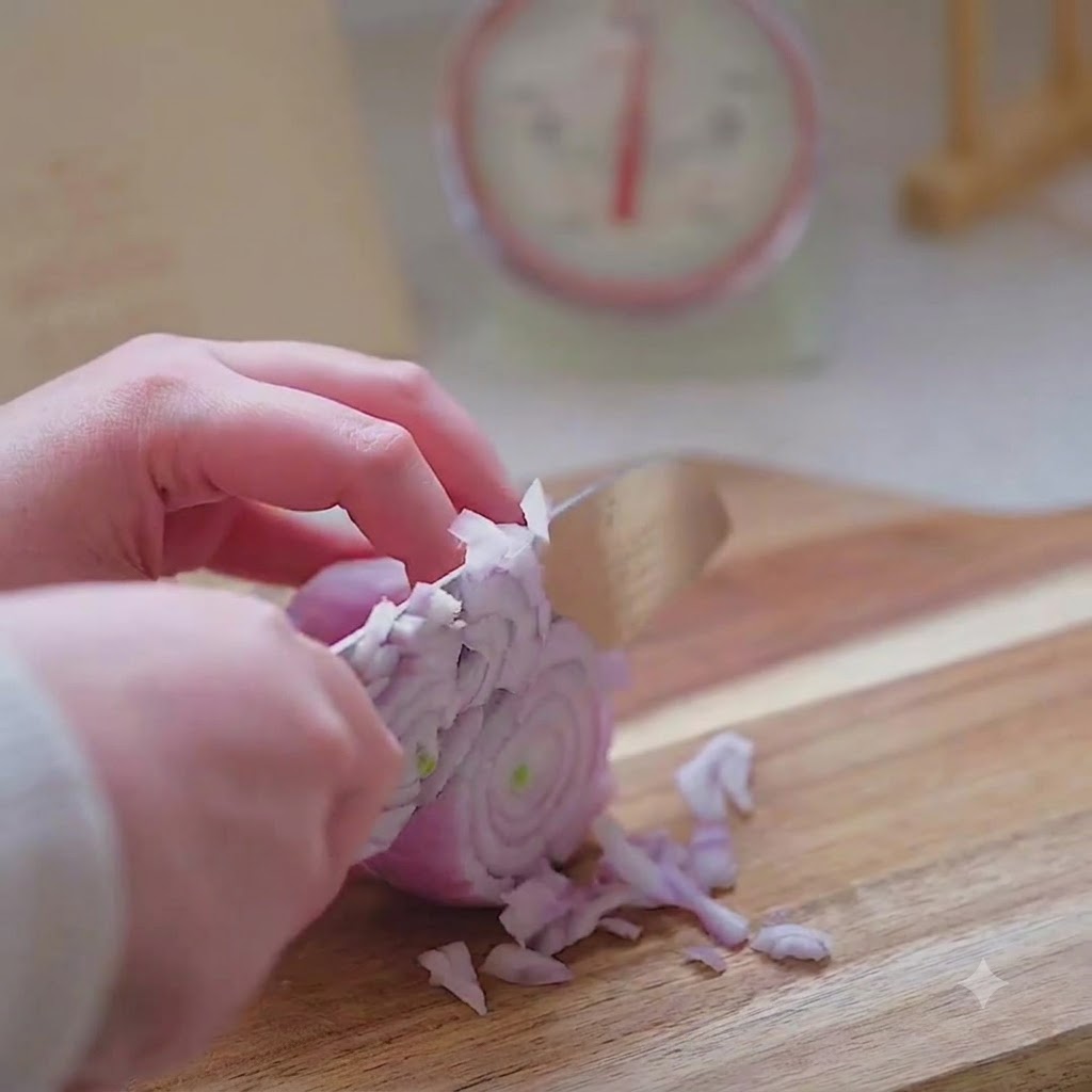A hand using a kitchen knife to carefully mince a red onion into fine pieces on a wooden board.