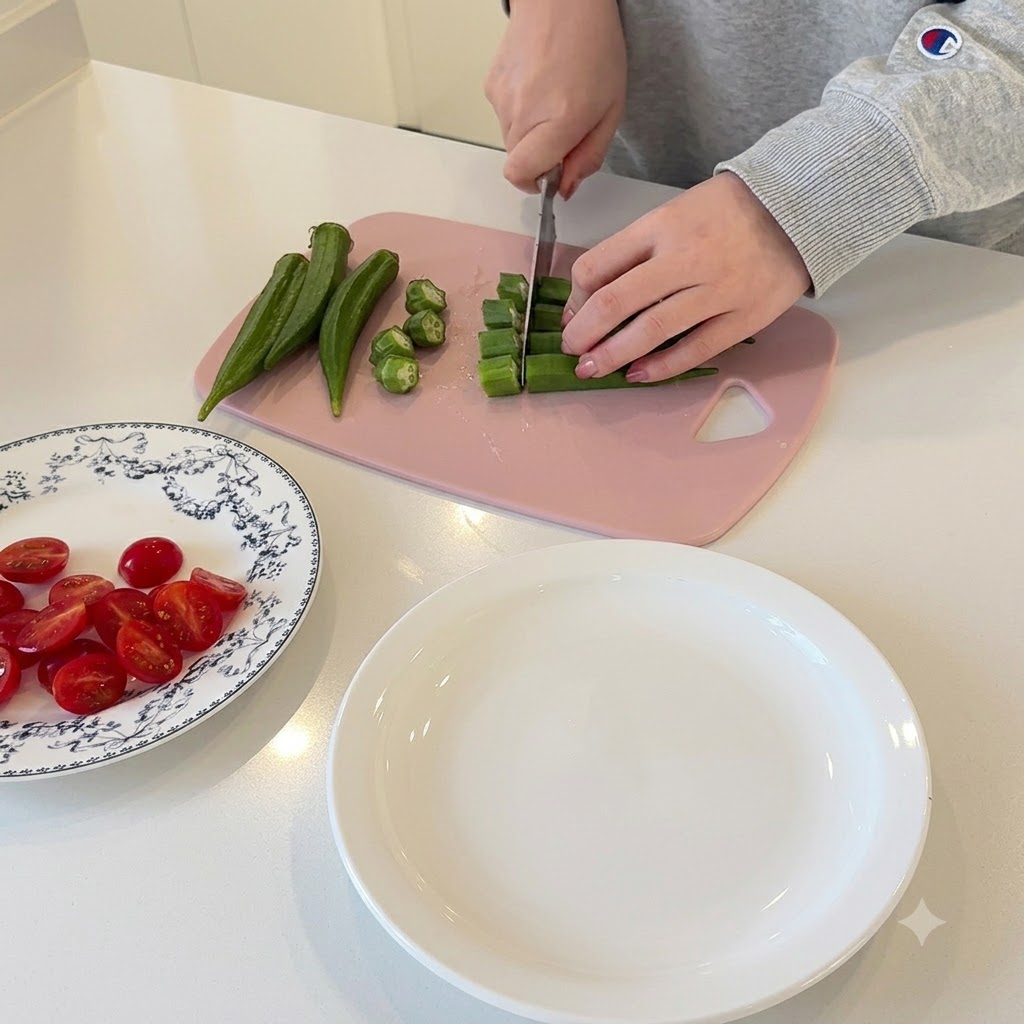 Hands slicing green okra into small circular pieces on a pink cutting board.