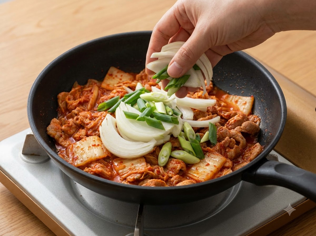 Sliced onions and green onions being added into the pot over the kimchi.