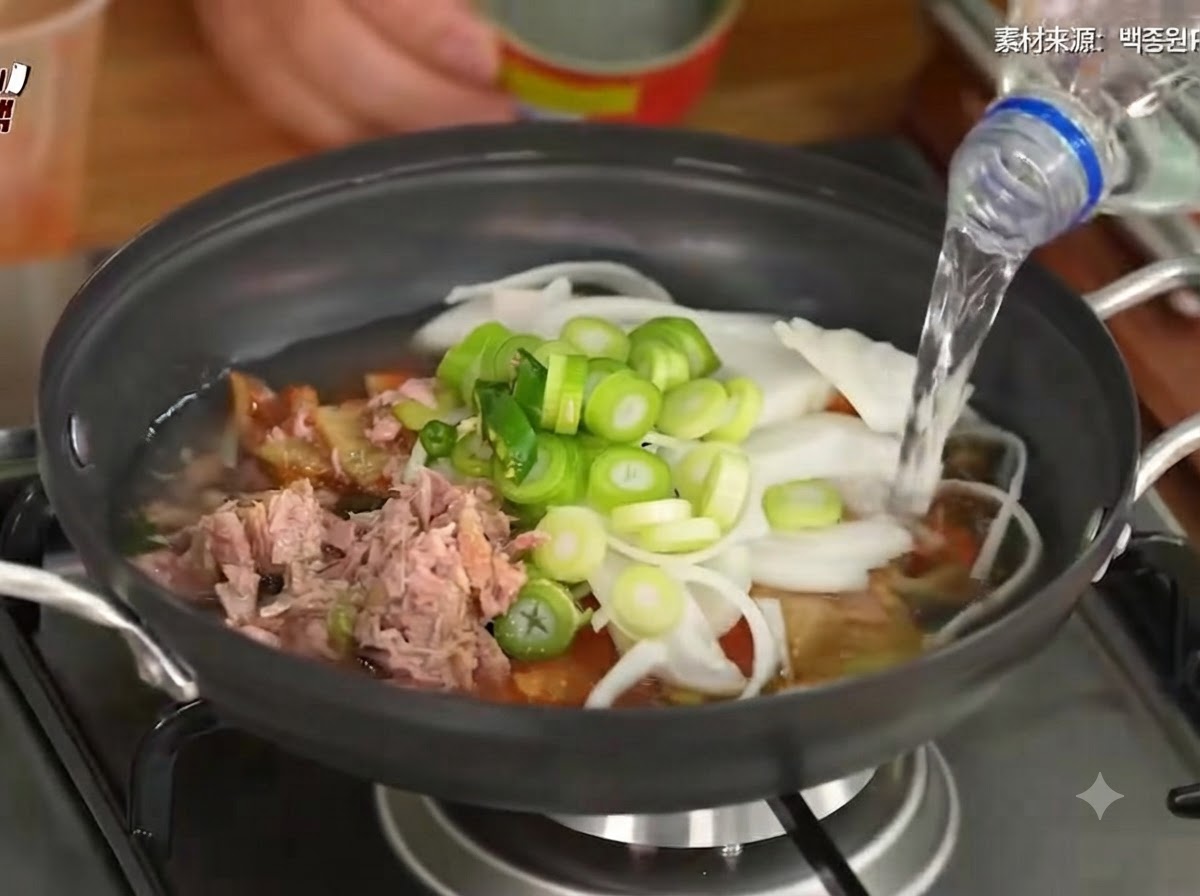 Water being poured into the pot containing kimchi, vegetables, and tuna.