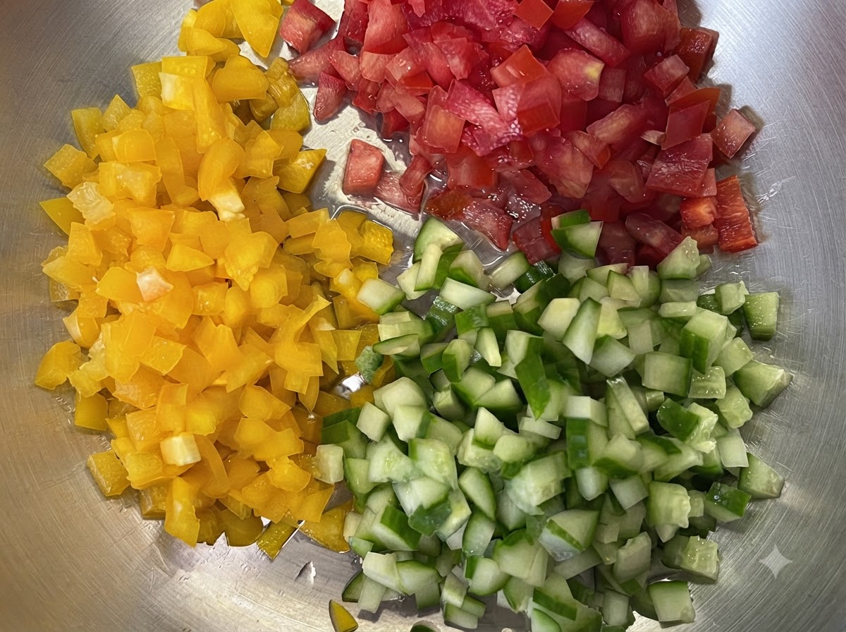 Yellow bell peppers, red tomatoes, and green cucumbers finely diced into small cubes on a tray.