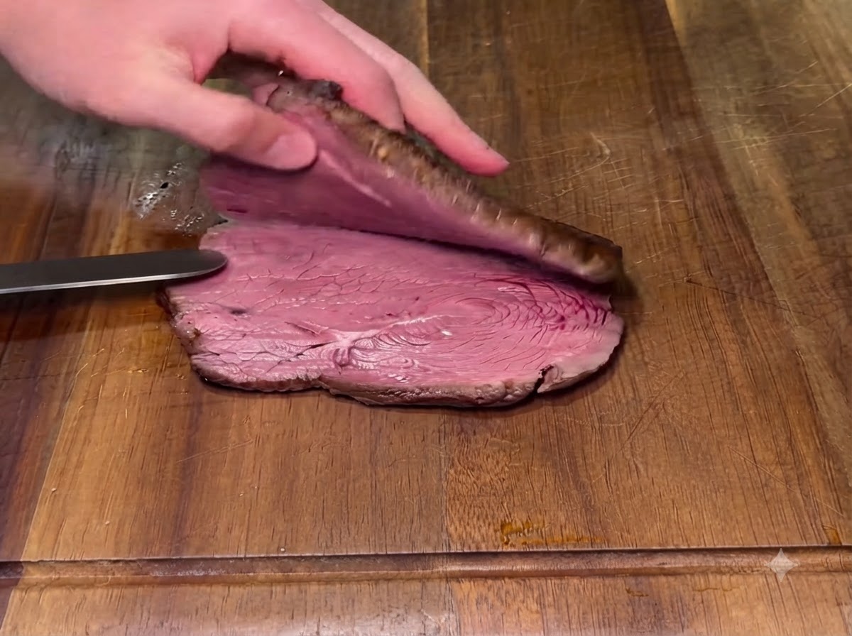 A cooked steak being sliced horizontally in half on a wooden cutting board with a knife.