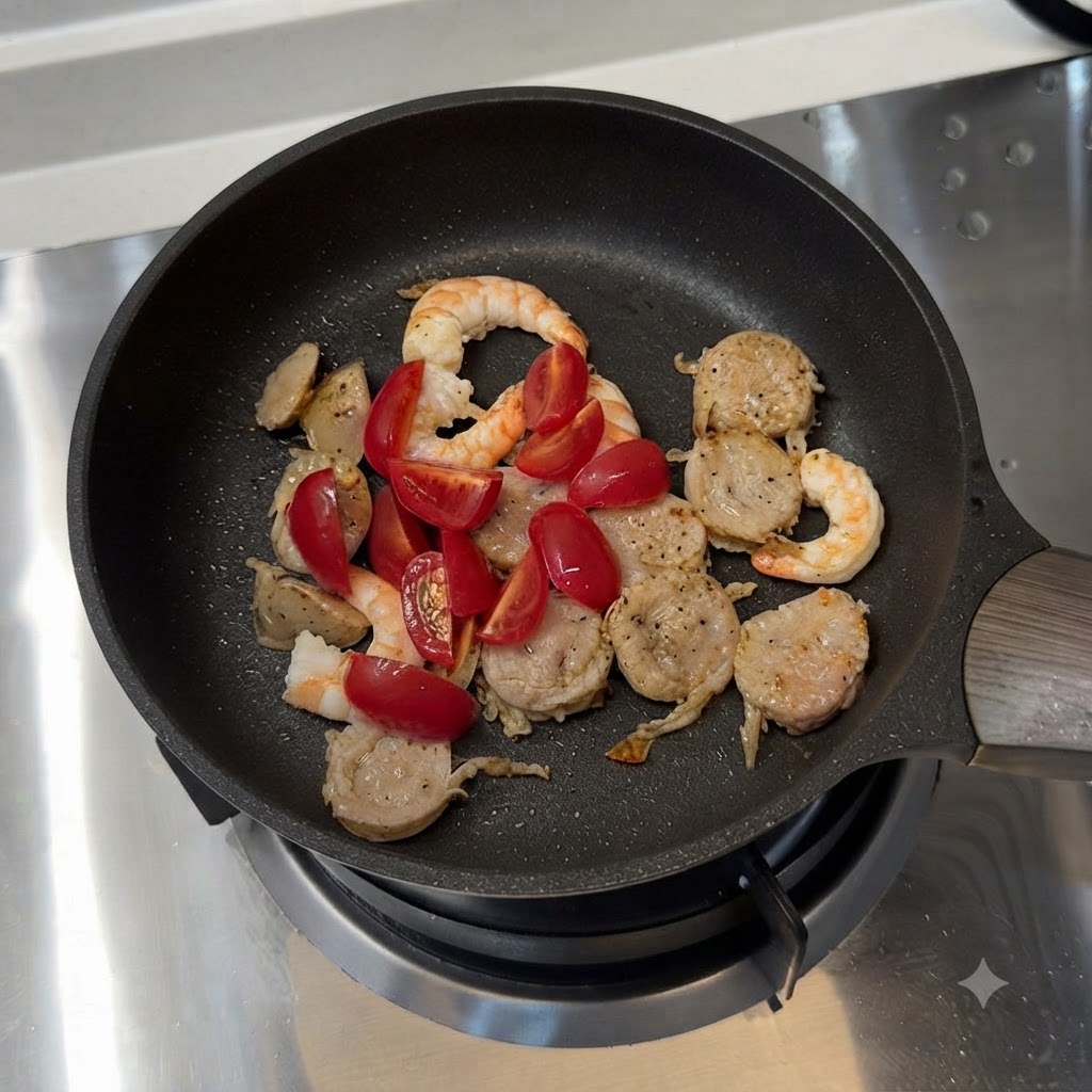 Cherry tomatoes and sliced green bell peppers mixed with sausage and shrimp in a frying pan.