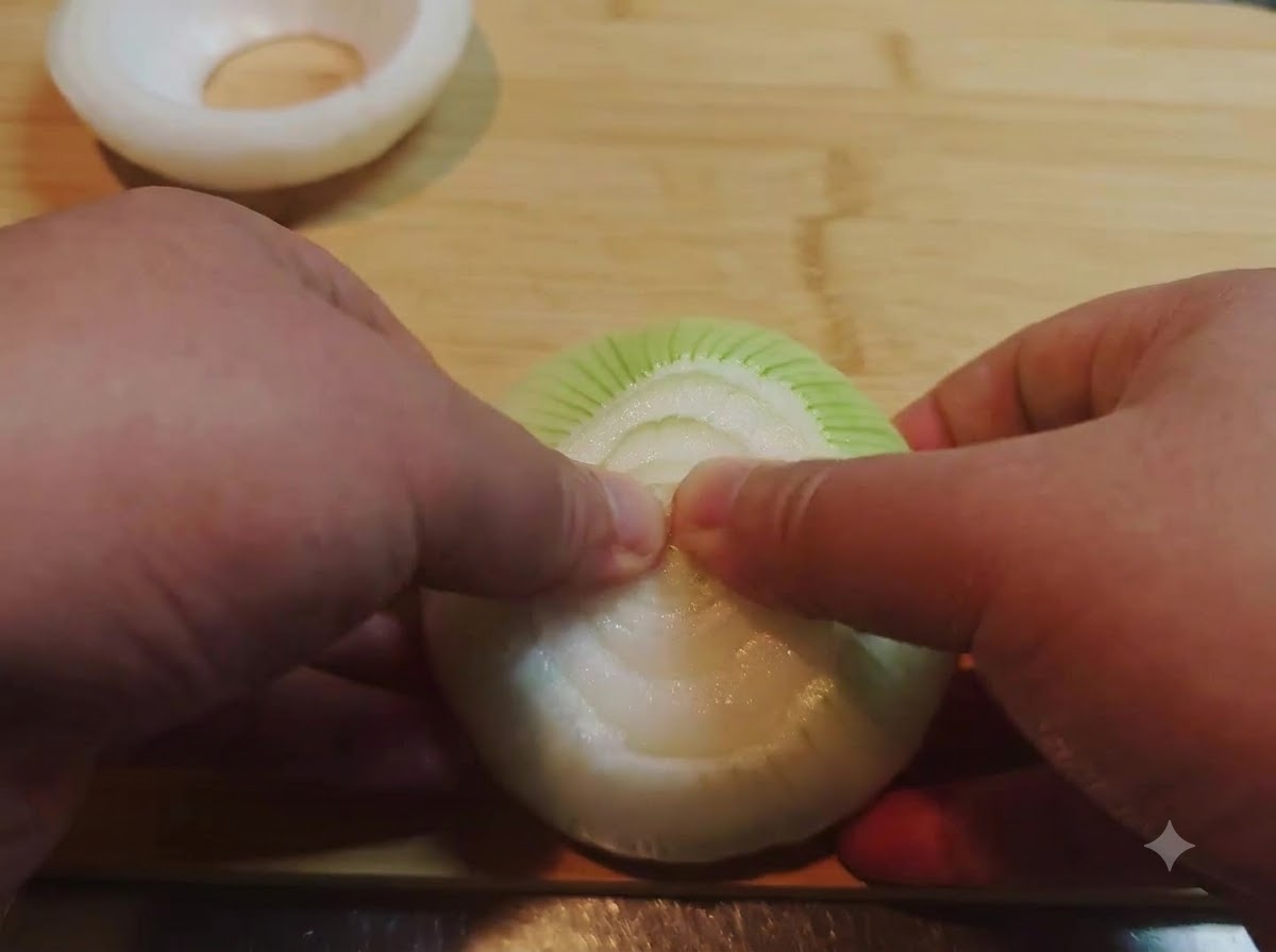 Hands pressing and removing the inner layers of an onion half to create a hollow onion ring.