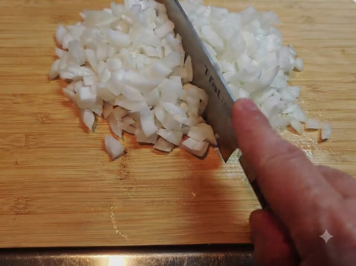 A pile of finely diced white onions being chopped with a knife on a bamboo cutting board.
