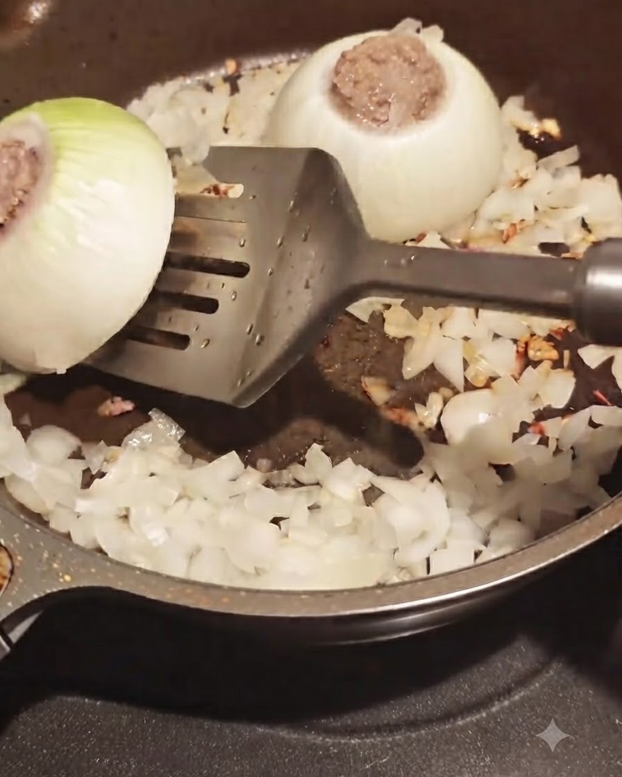 A spatula flipping a meat-stuffed onion ring in a frying pan with surrounding chopped onions.