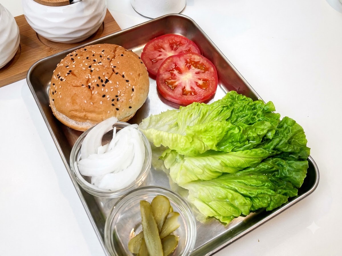 A gloved hand sprinkling salt over raw chicken pieces arranged in a stainless steel tray.