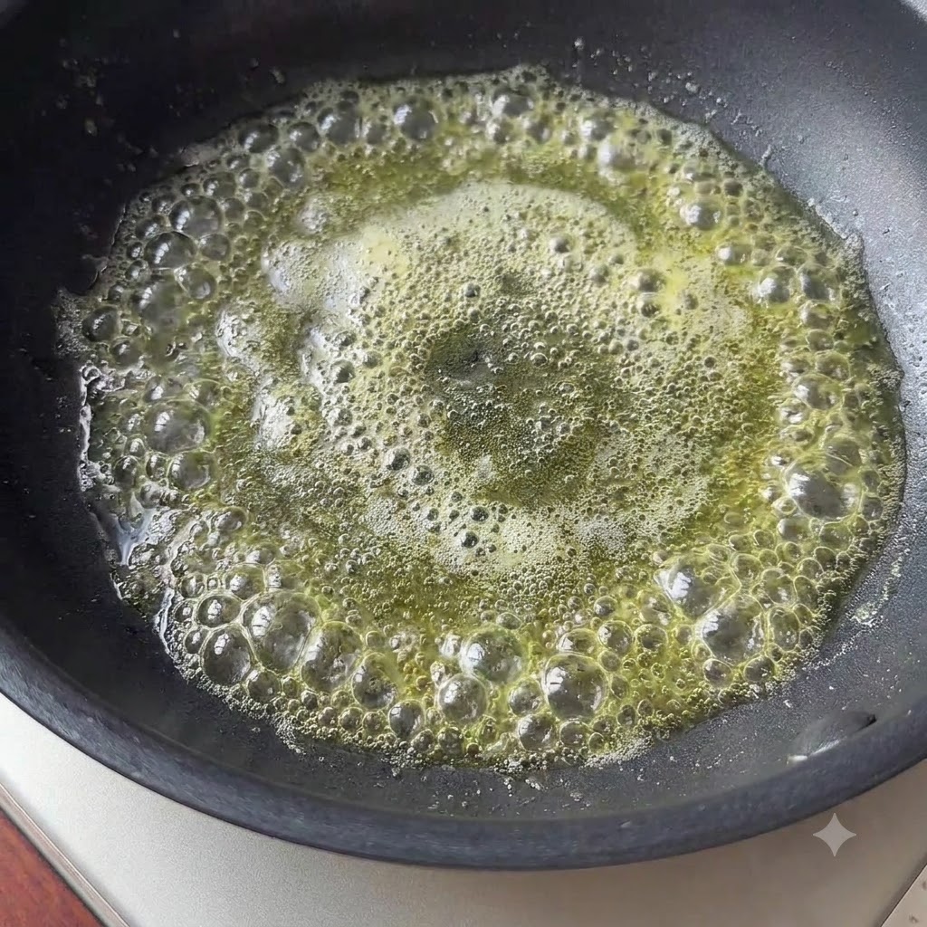 A small piece of butter melting and bubbling in a black skillet.