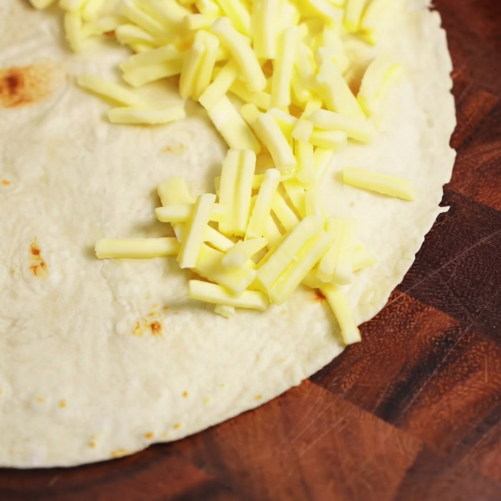 Cooked beef filling and mozzarella cheese being arranged on one half of a flat flour tortilla.