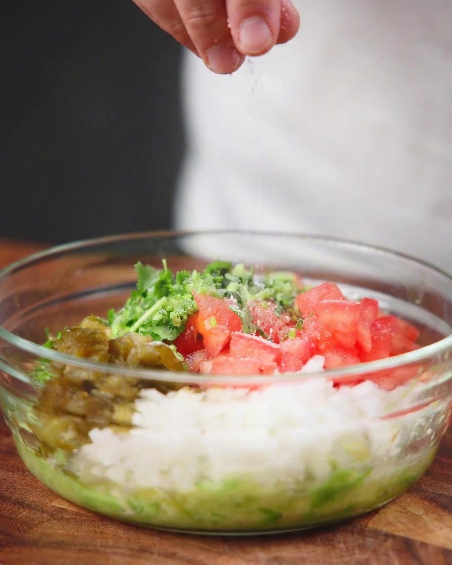 Sea salt being sprinkled from above into a clear glass bowl filled with chopped tomatoes, onions, peppers, and herbs.
