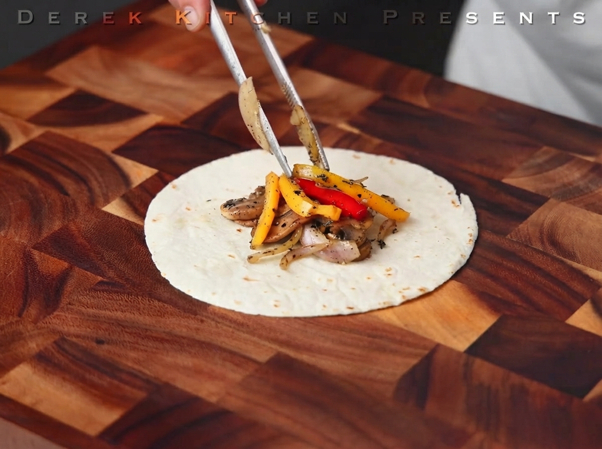 Cooked steak being cut into strips on a wooden board.