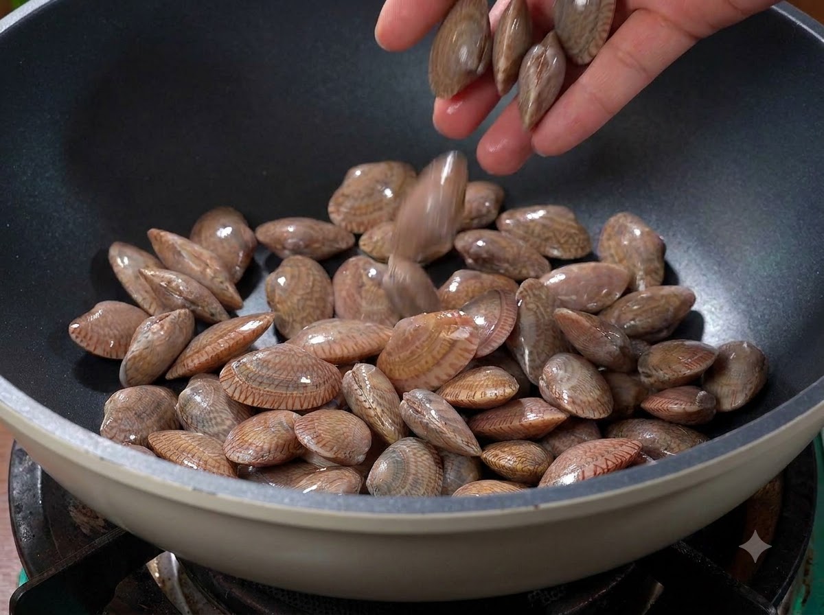 Clams being tossed into a hot dry wok on the stove.