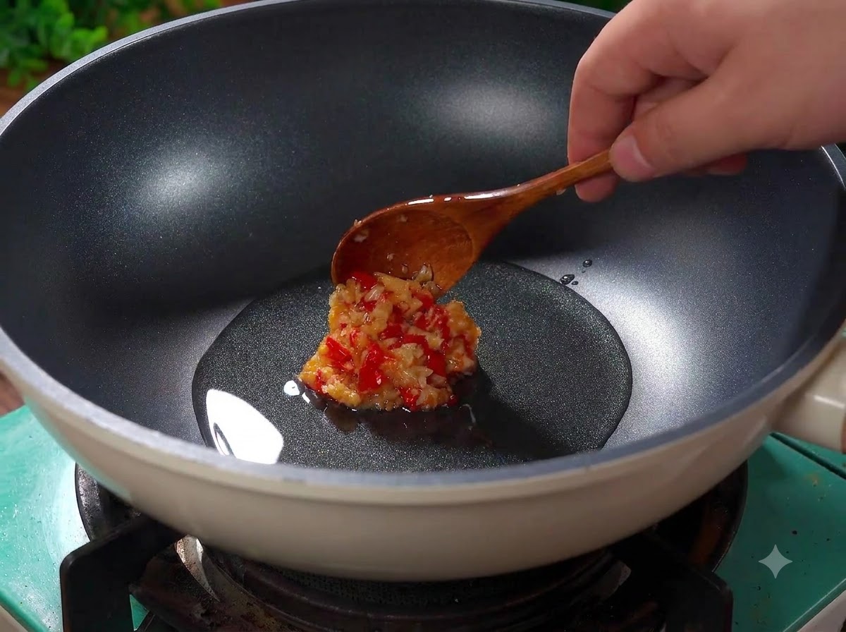Minced garlic and chopped red chilies sizzling in hot oil inside a wok.