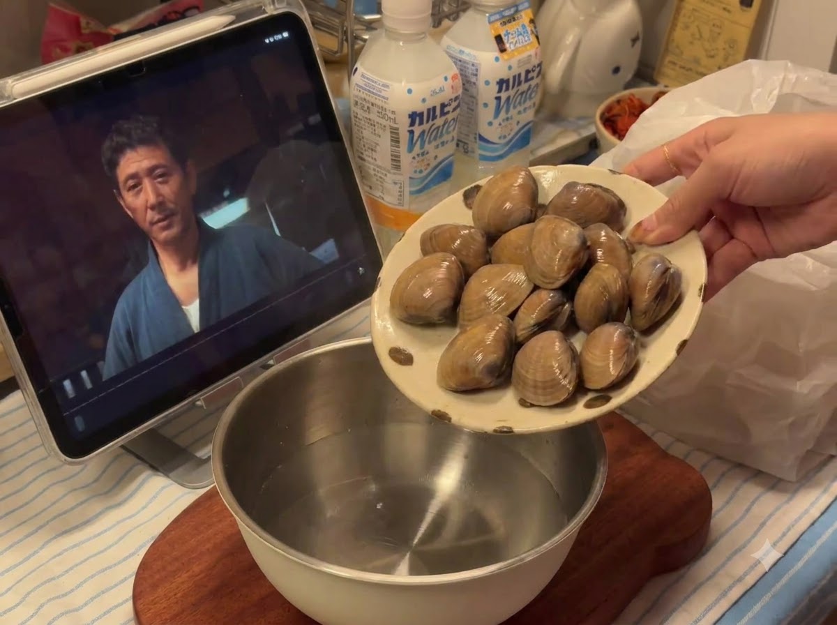 Fresh clams being poured from a plate into a metal bowl containing water.