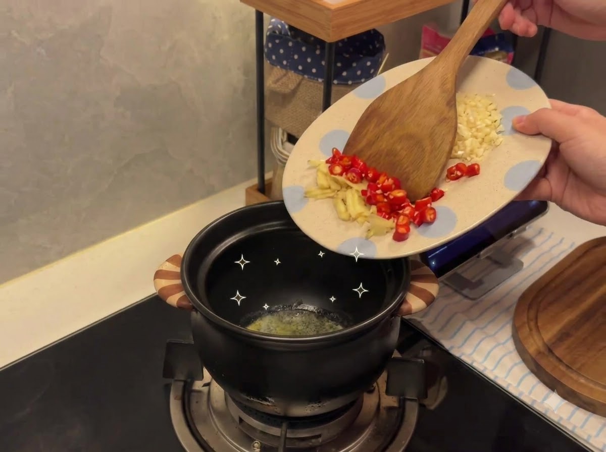 Minced garlic and chili peppers being transferred from a patterned plate into a ceramic pot containing melted butter.