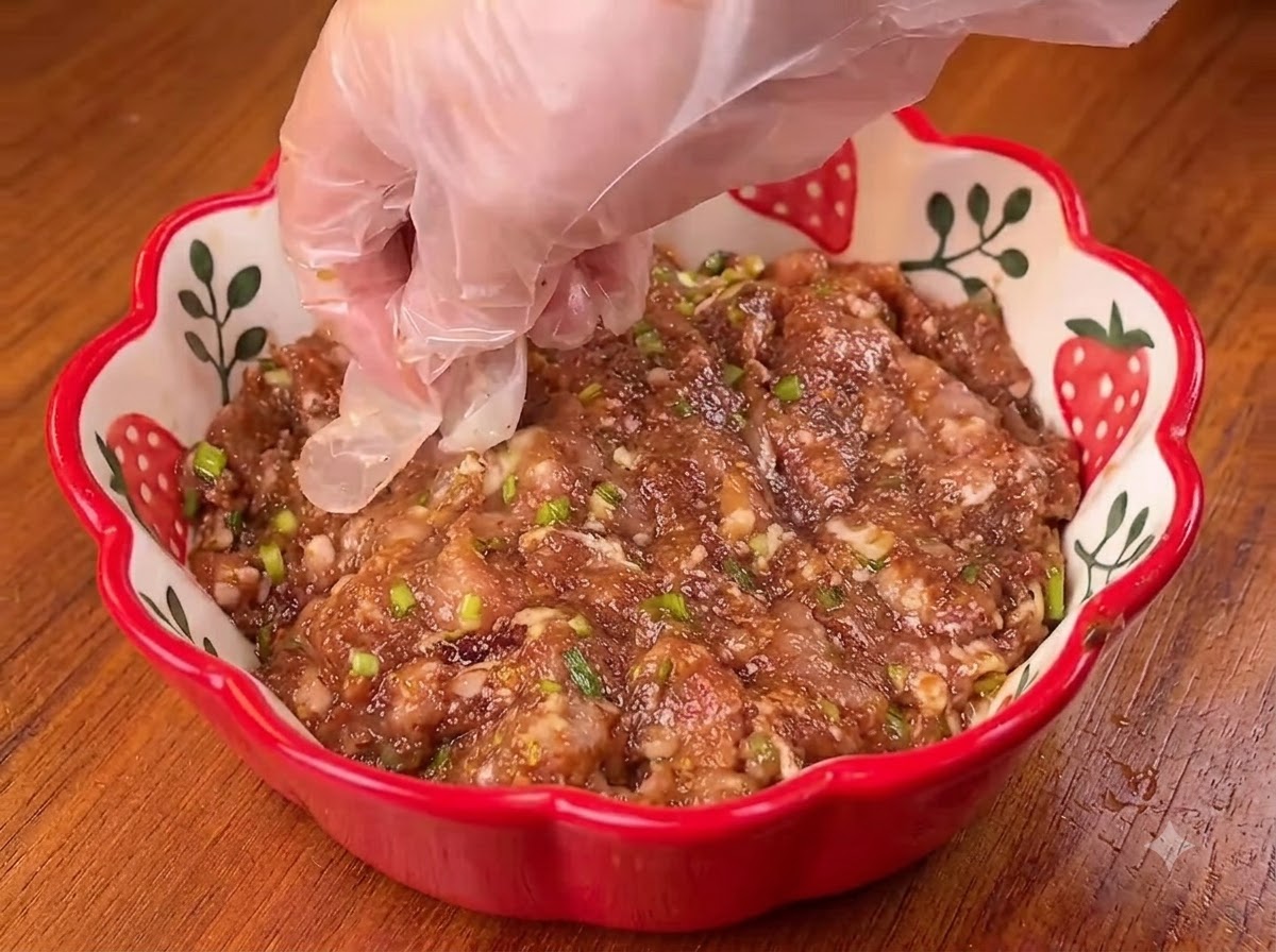 A wooden rolling pin flattening a round piece of scallion pancake dough on a wooden board.