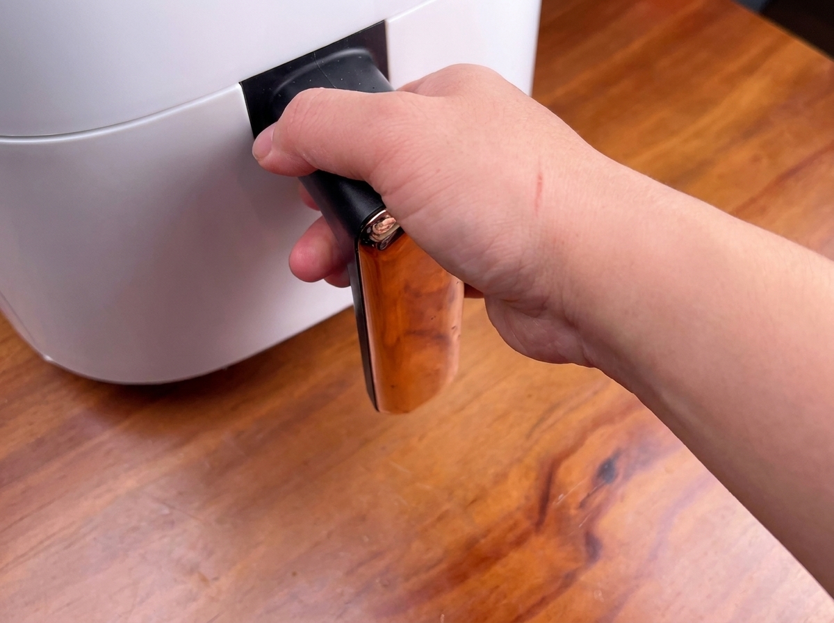 A person holding the handle of a white air fryer, about to slide the basket in.