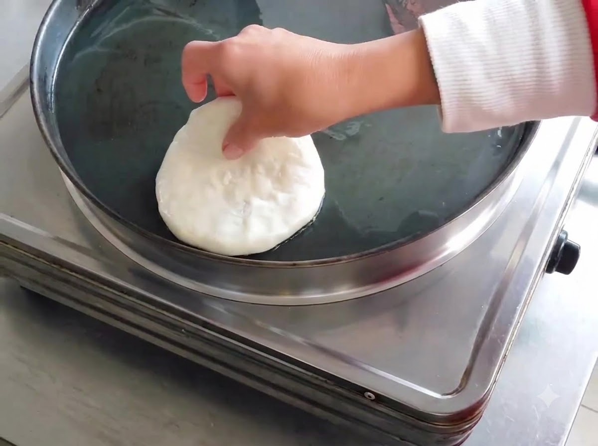 A raw shaped meat pie being placed into an oiled electric skillet.