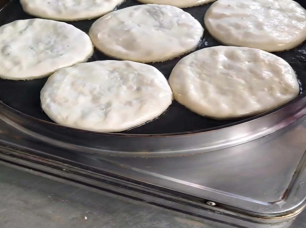Several round meat pies cooking in a skillet with oil drizzled on top.