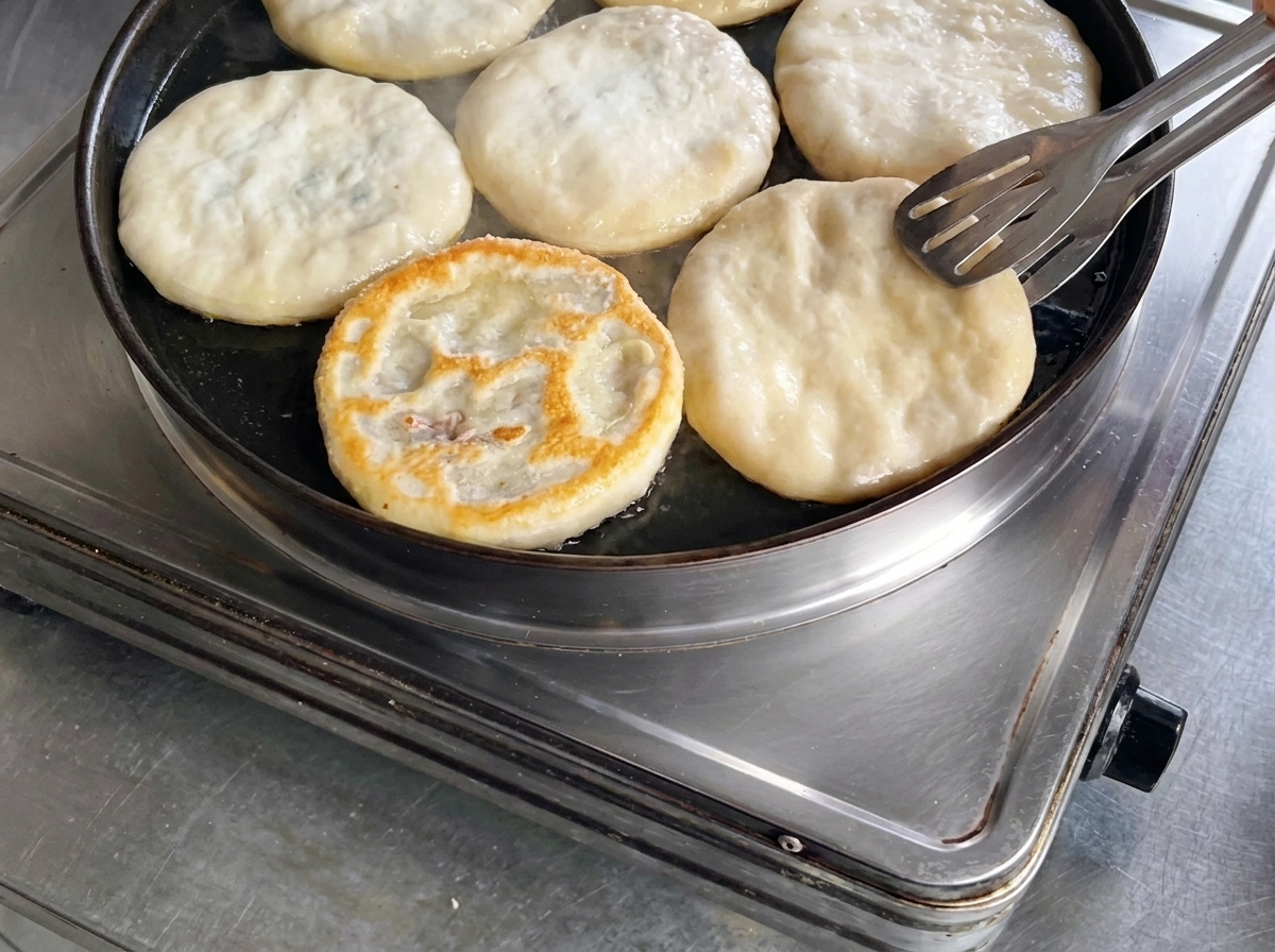 Using metal tongs to flip a meat pie in a skillet, revealing a perfectly browned and crispy top surface.