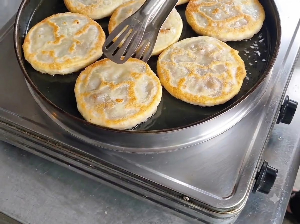 Golden-brown cooked meat pies being checked with tongs in the skillet before removal.