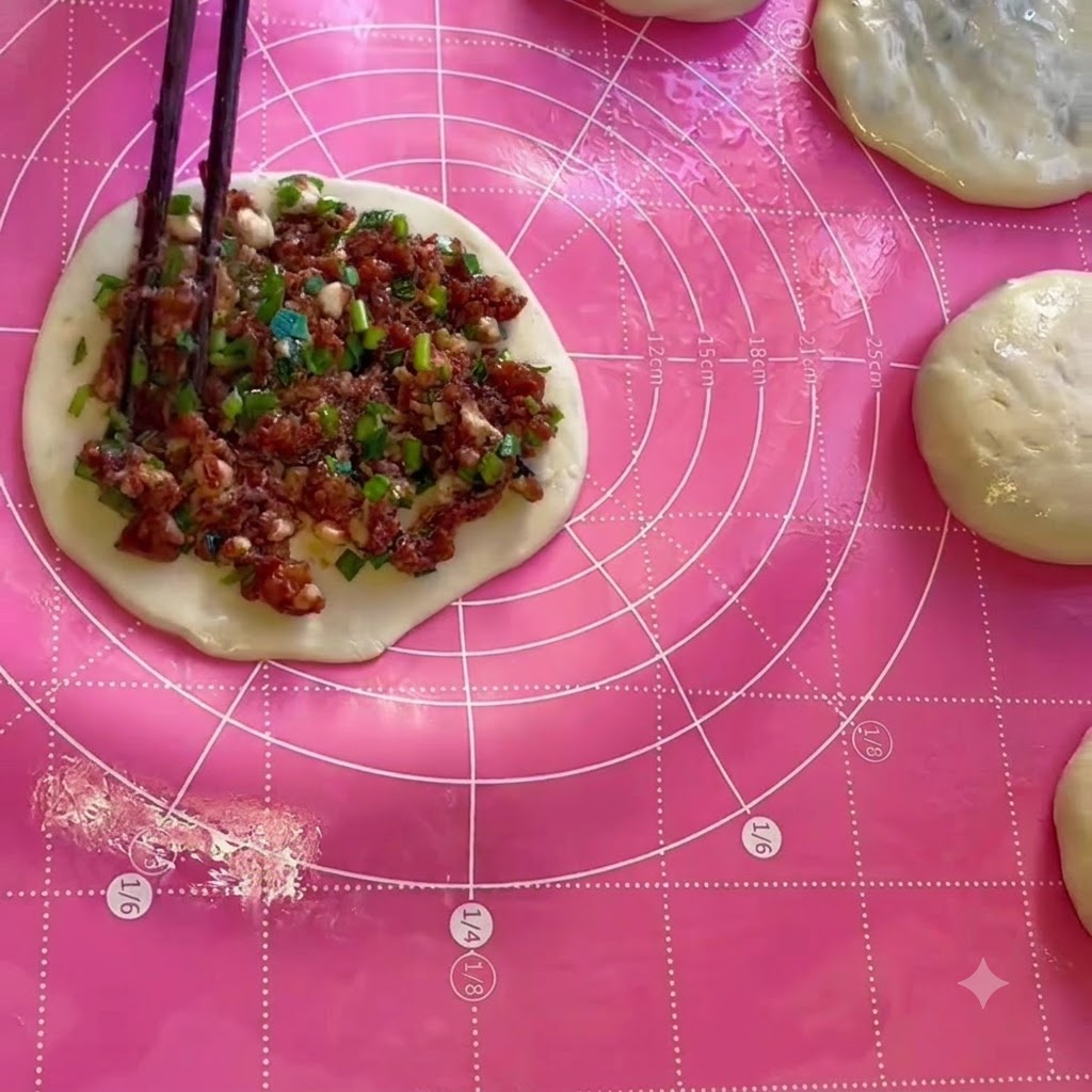 Meat and chive filling being spread evenly onto a circular sheet of dough using chopsticks.