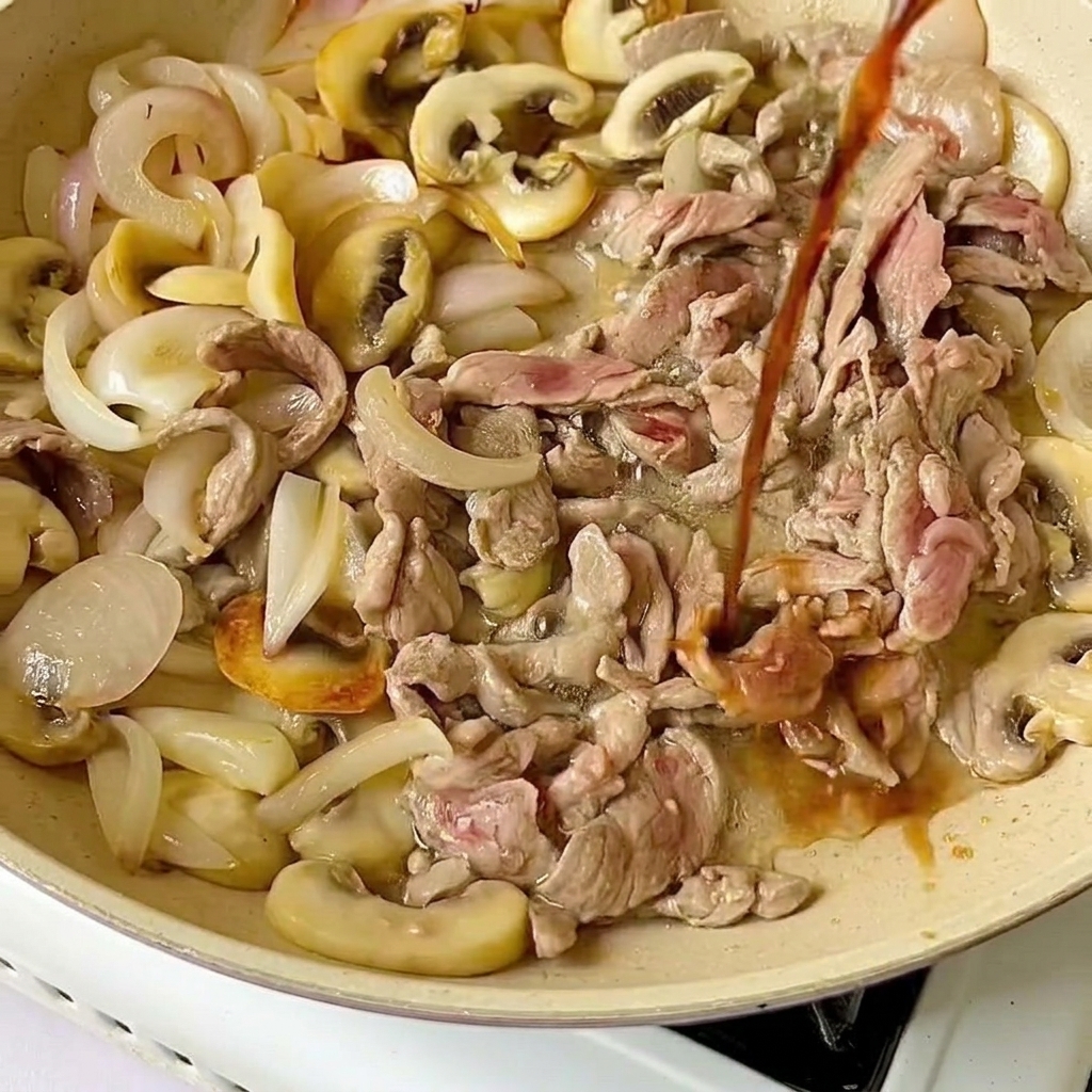Light soy sauce being drizzled from above onto raw beef slices and cooked vegetables in a pan.