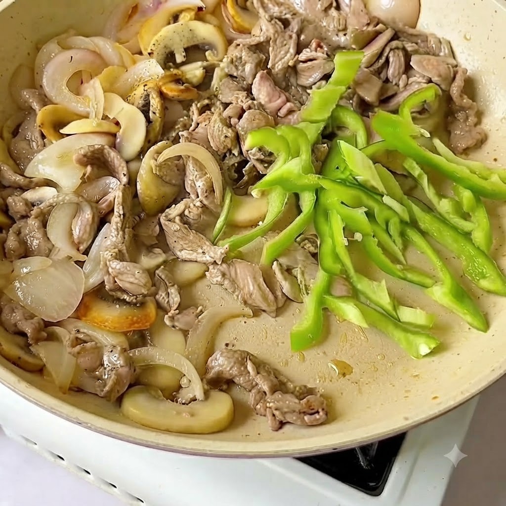 Fresh green pepper slices added to the frying pan alongside beef and onions.