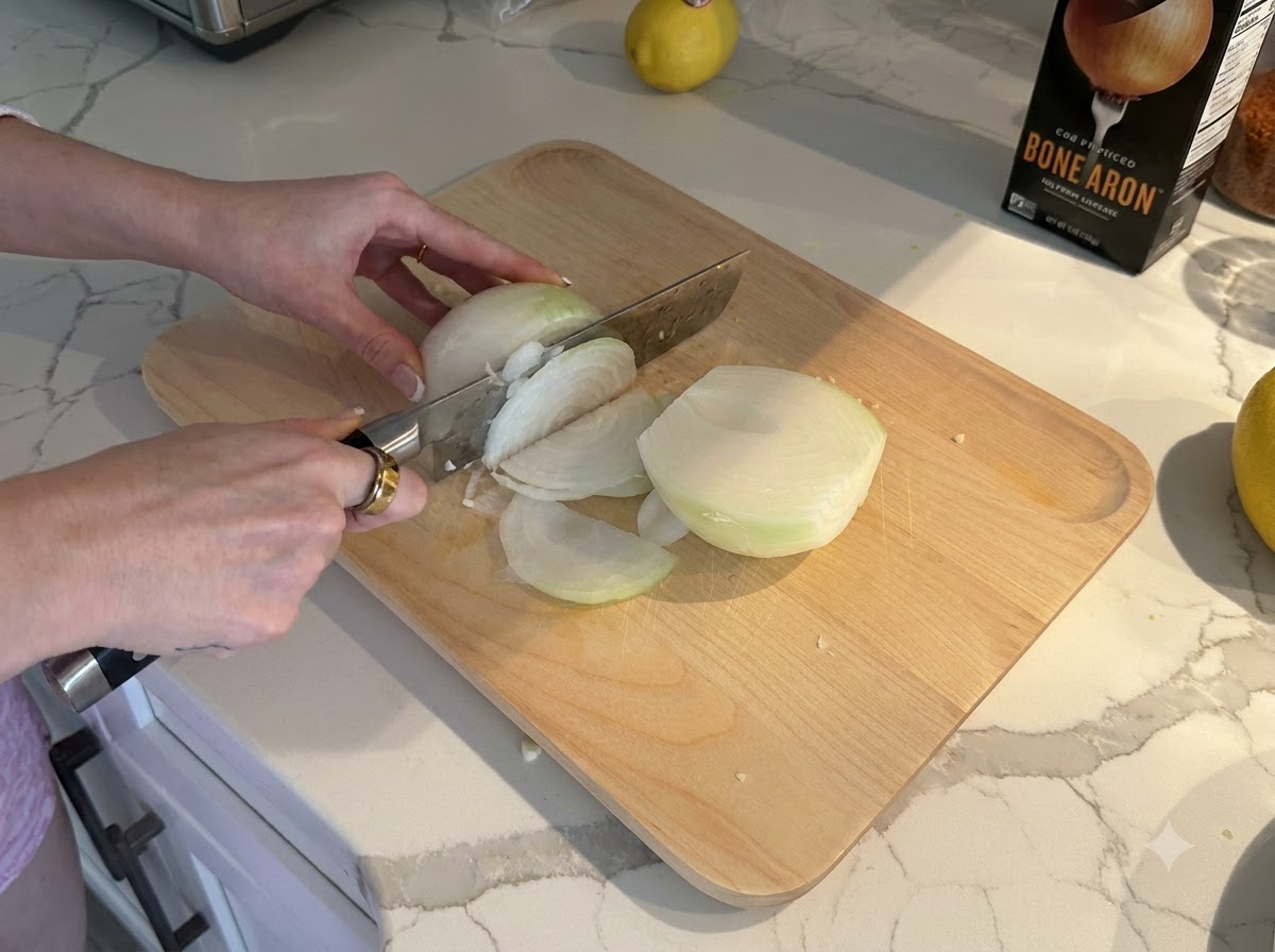 A white onion being sliced and diced into small pieces on a wooden cutting board.