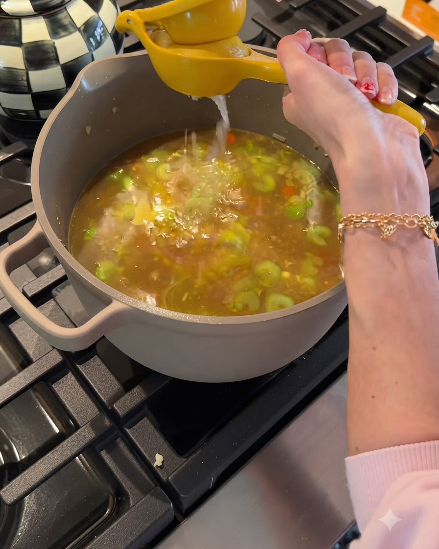 Squeezing fresh lemon juice from a yellow citrus press into a pot of simmering chicken broth and vegetables.