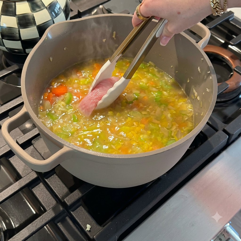 Raw chicken breast fillets being placed into a pot of bubbling vegetable and bone broth using silicone-tipped tongs.