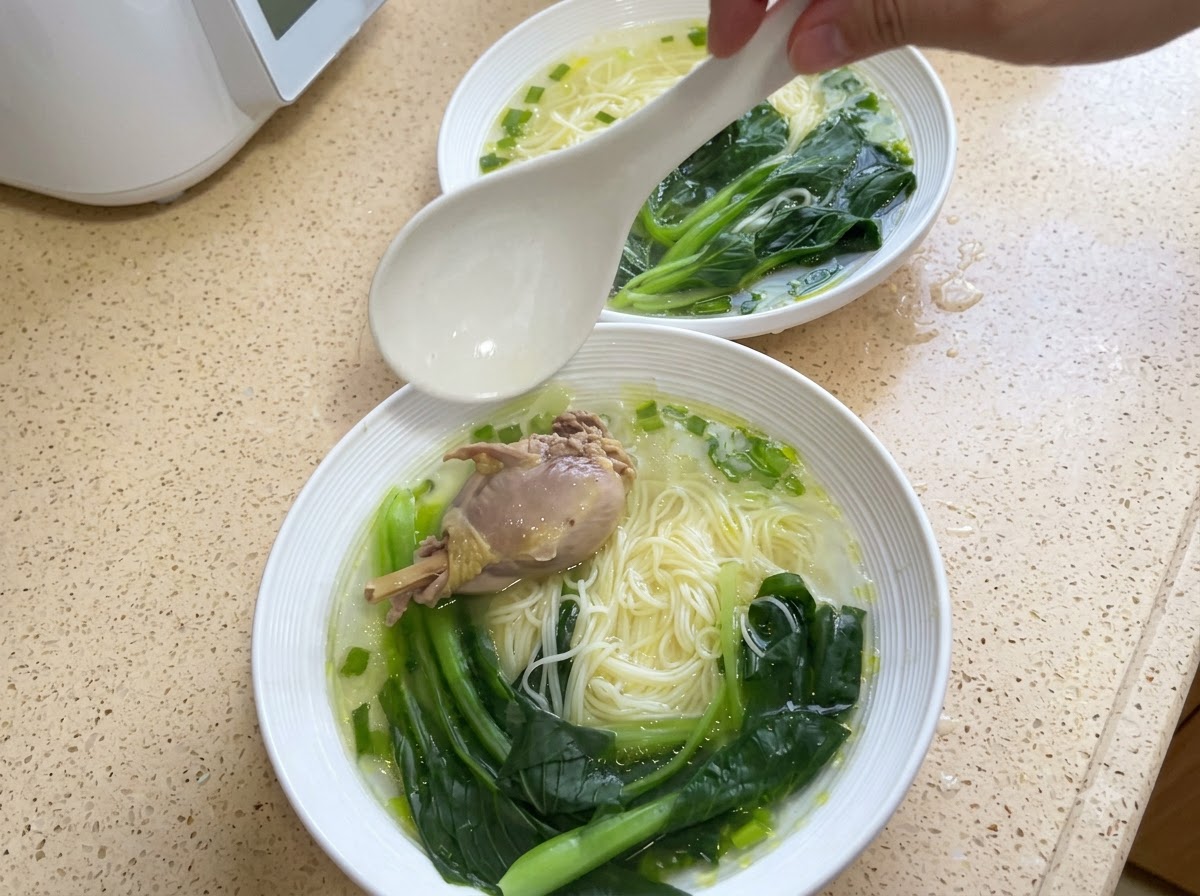 A bowl of noodles topped with a piece of chicken and cooked bok choy.