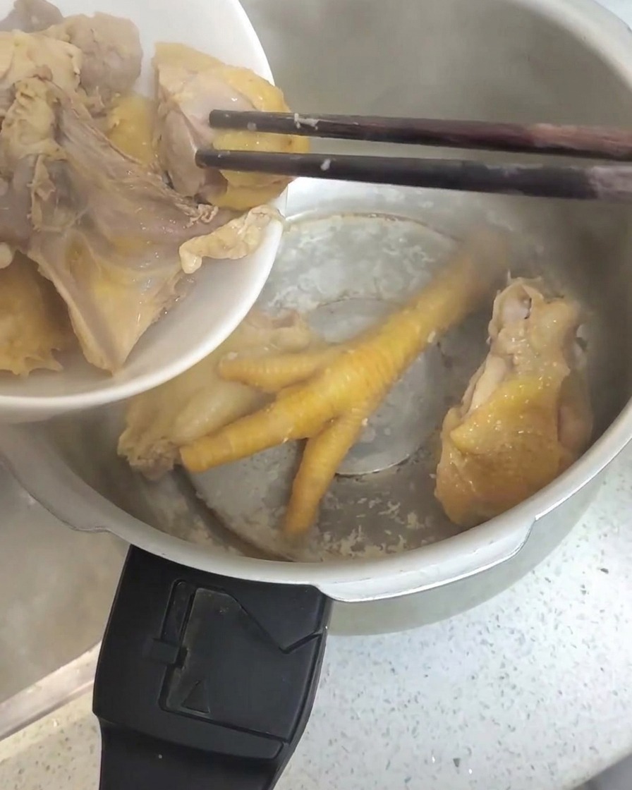 Blanched chicken pieces being transferred with chopsticks into a stainless steel pressure cooker.
