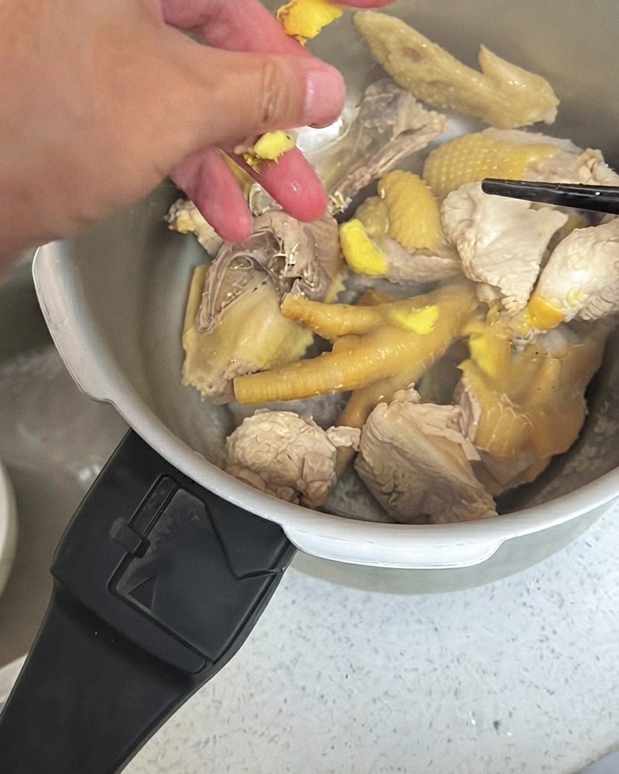 Smashed ginger pieces being scattered over chicken inside a pressure cooker.