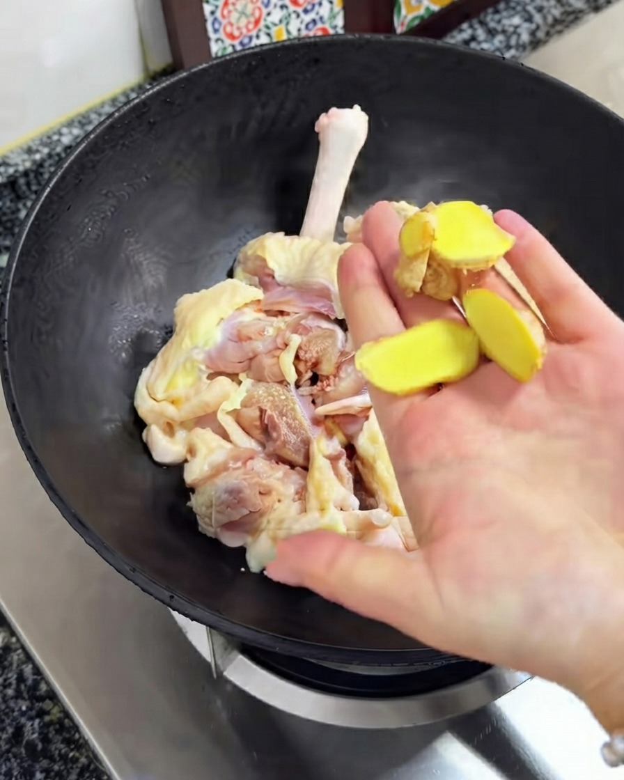 Fresh ginger slices being held above the raw chicken inside the black wok.