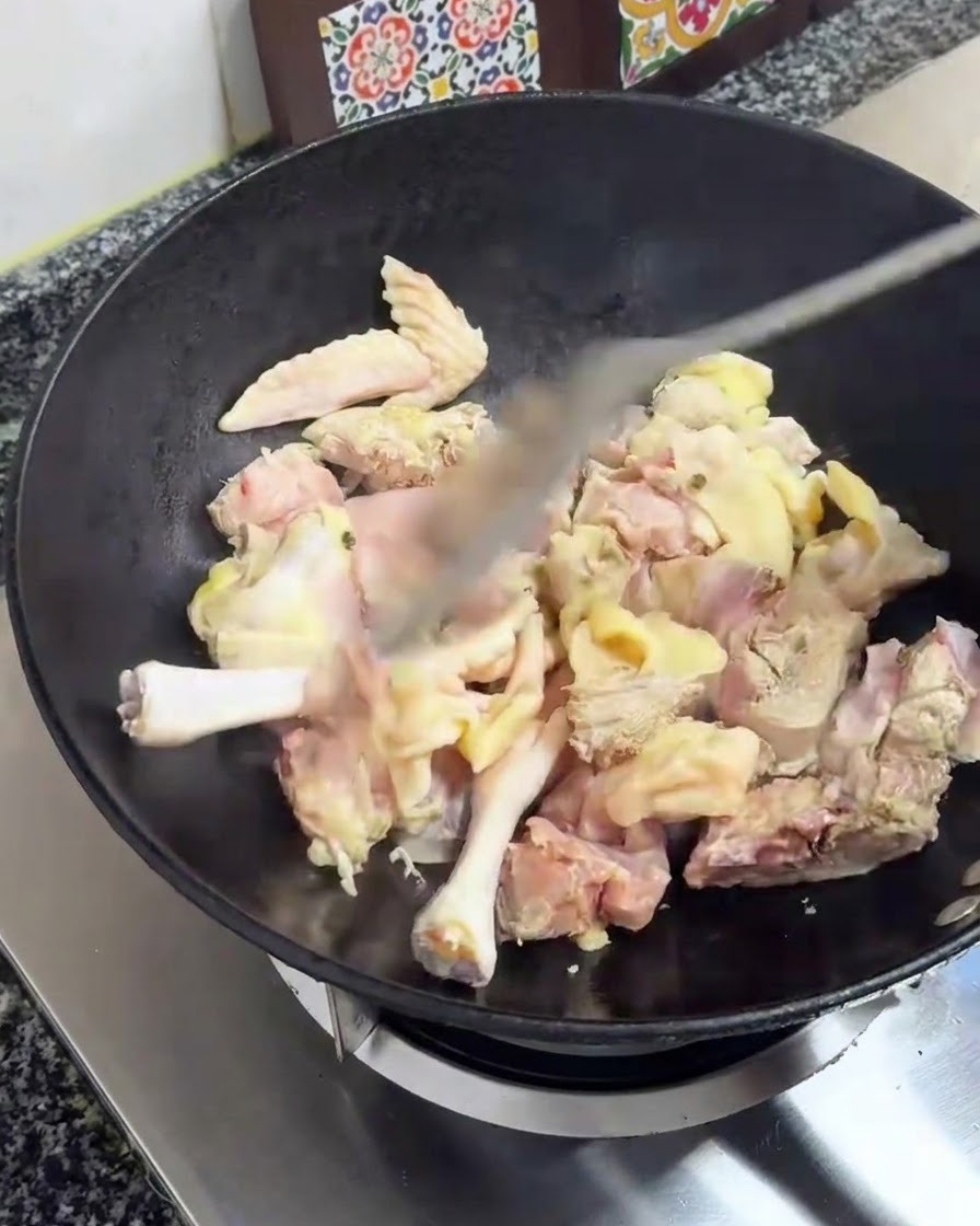 Chicken pieces being stir-fried with a spatula in a black wok over a stove.