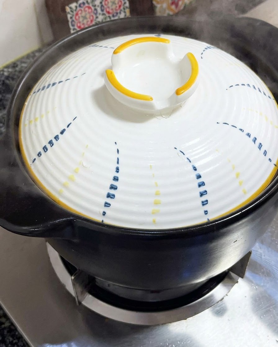 A white lid with blue and yellow patterns being placed firmly on top of a black clay pot.